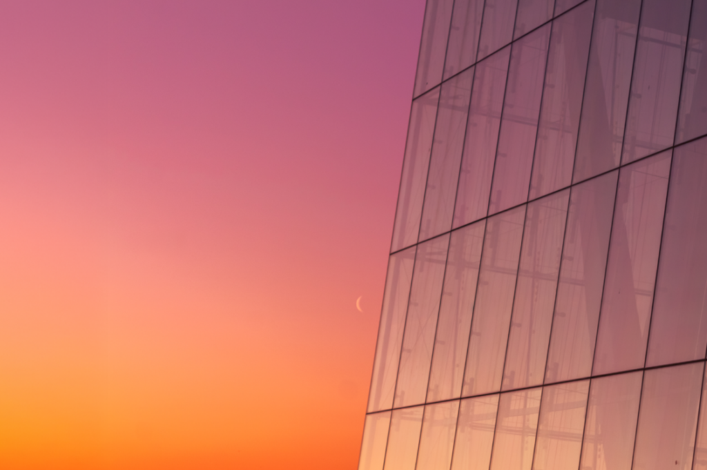 Off-center, zoomed-in capture of a glass skyscraper amid pink-orange sunset backdrop (Source: Getty Images)