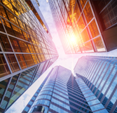 Abstract, golden facade of office buildings as sunlight peeks through as lens is angled upward from below (source: Getty Images)
