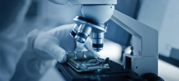 Close-up of a scientist wearing coverall and gloves zoomed in on the gloved hands as they use a microscope to inspect a sample (source: Getty Images)